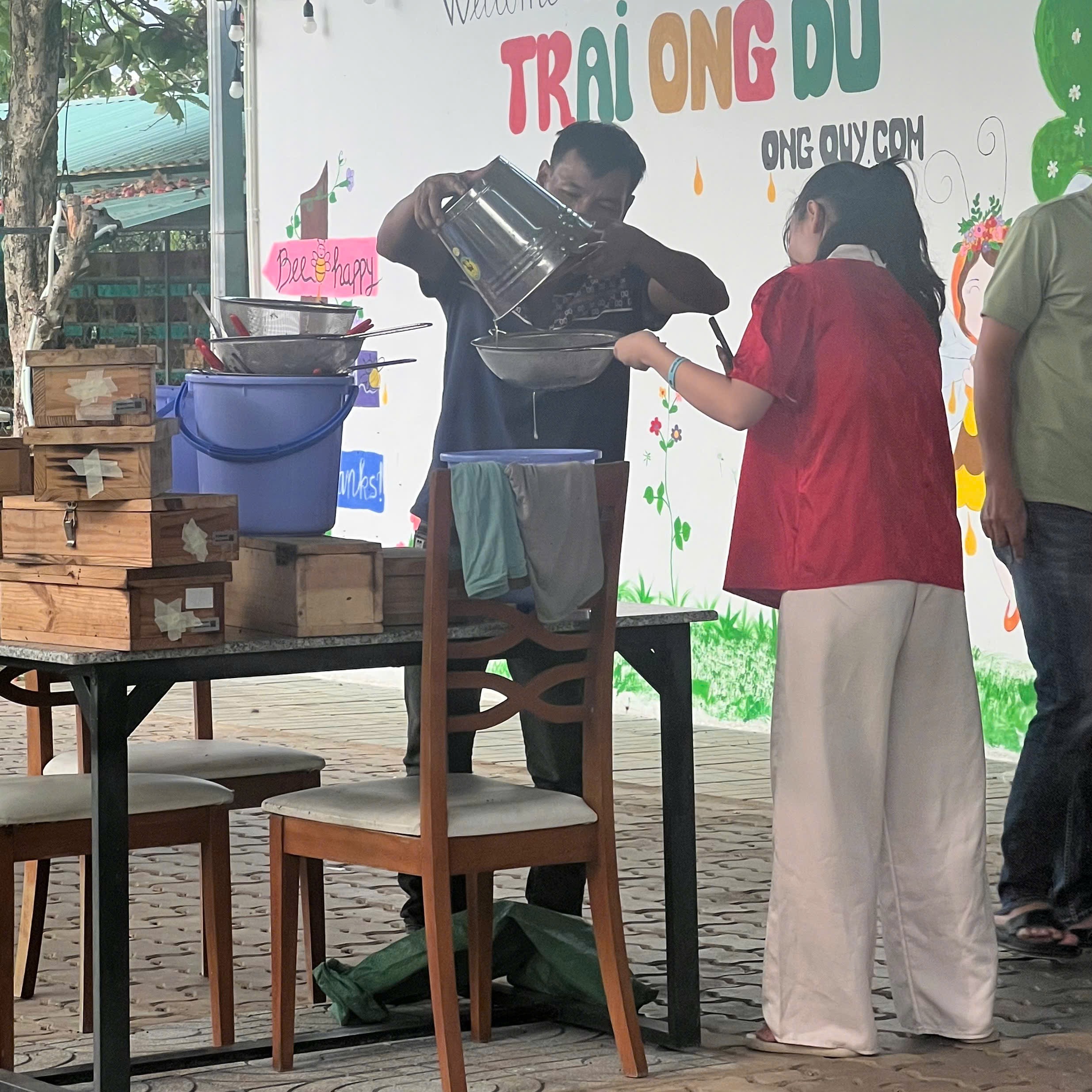 Thu mật ong dú thủ công tại trại OngMoc — lọc qua rây inox vào thùng đựng